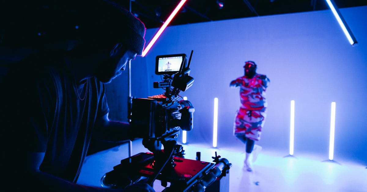 Filmfotograf bak et kamera under et innholdsopptak i et studio med blå og rosa neonlys